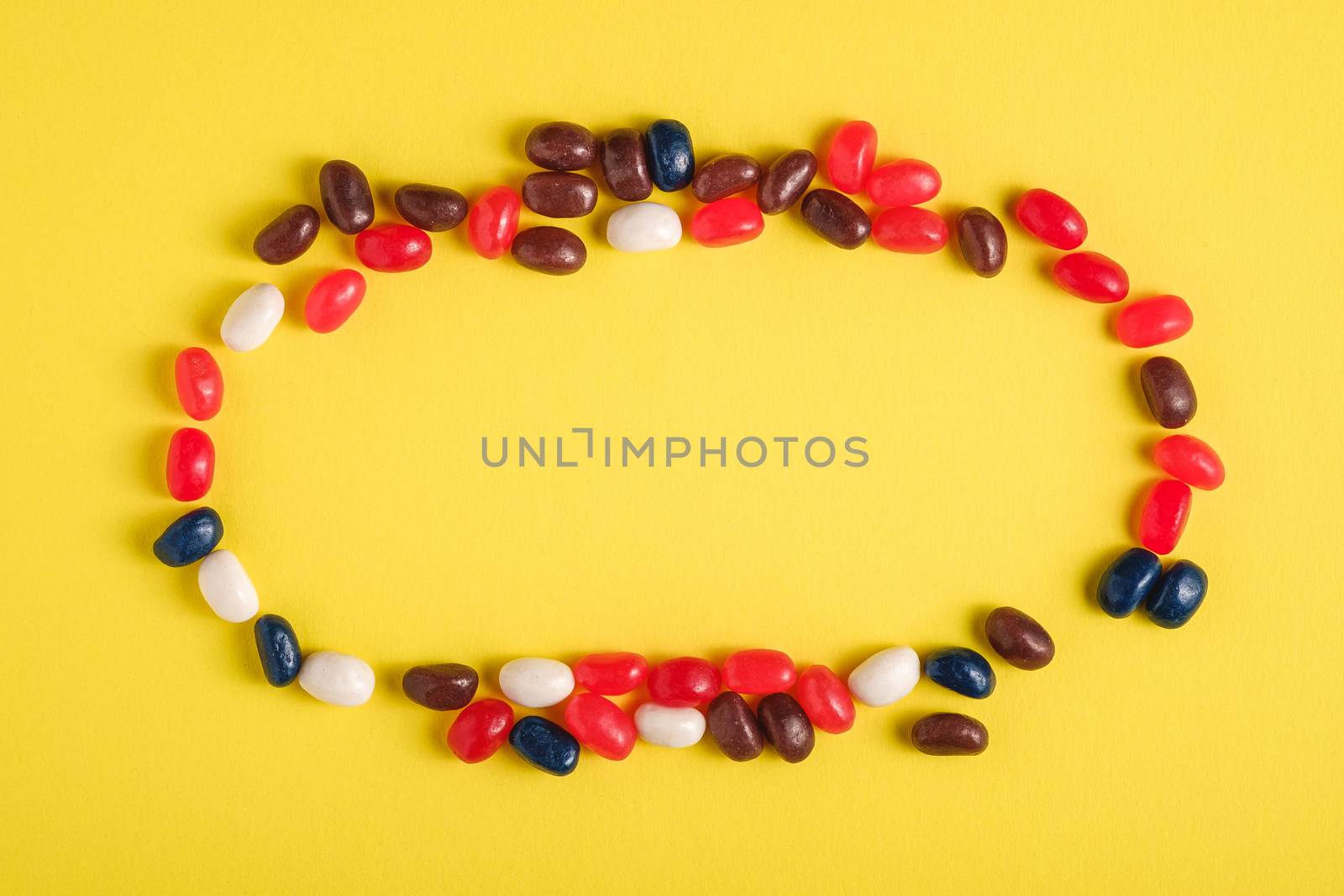 Round frame of juicy sweet fruit colorful jelly beans on bright yellow background, top view copy space
