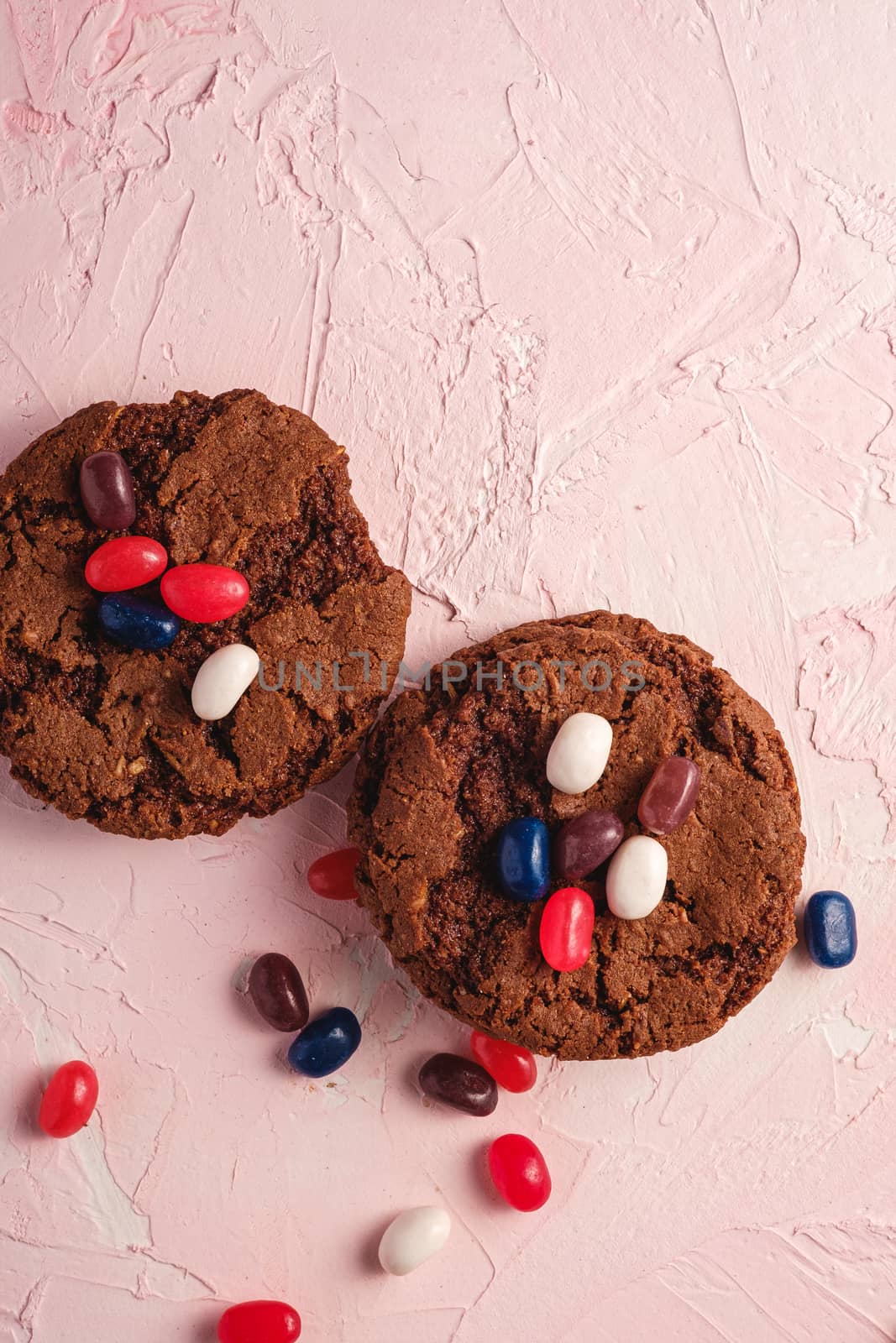 Homemade oat chocolate cookies with cereal with juicy jelly beans on textured pink background, top view copy space