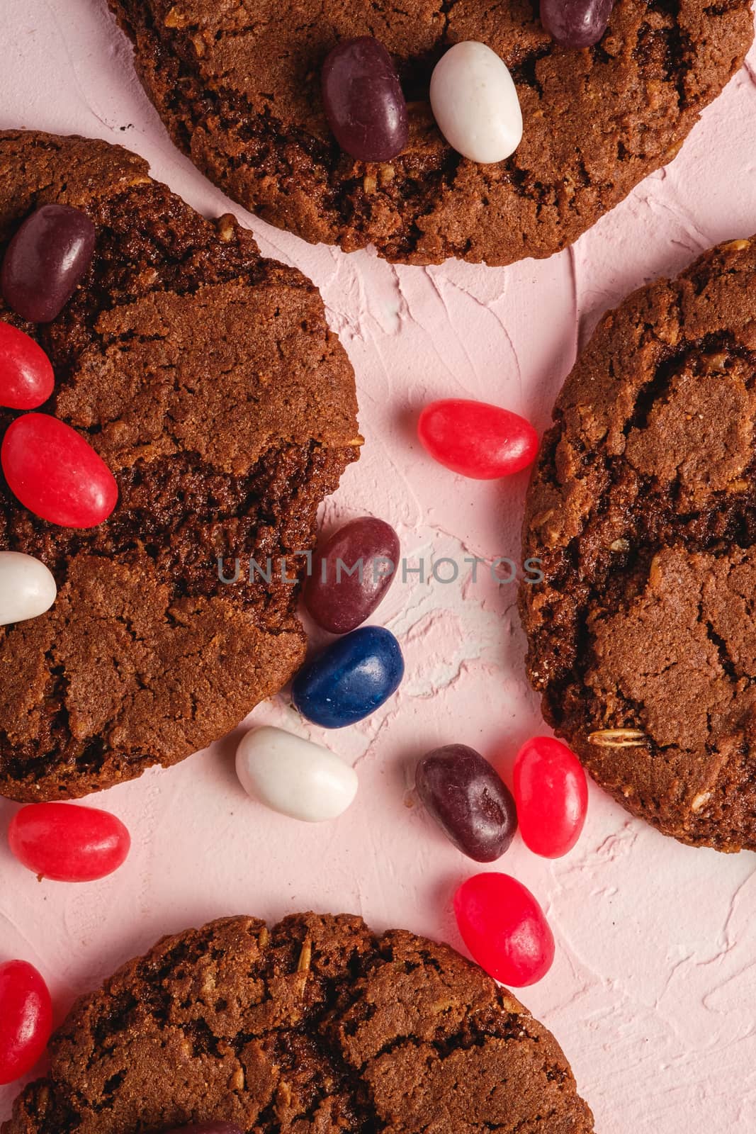 Homemade oat chocolate cookies with cereal with juicy jelly beans on textured pink background, top view macro