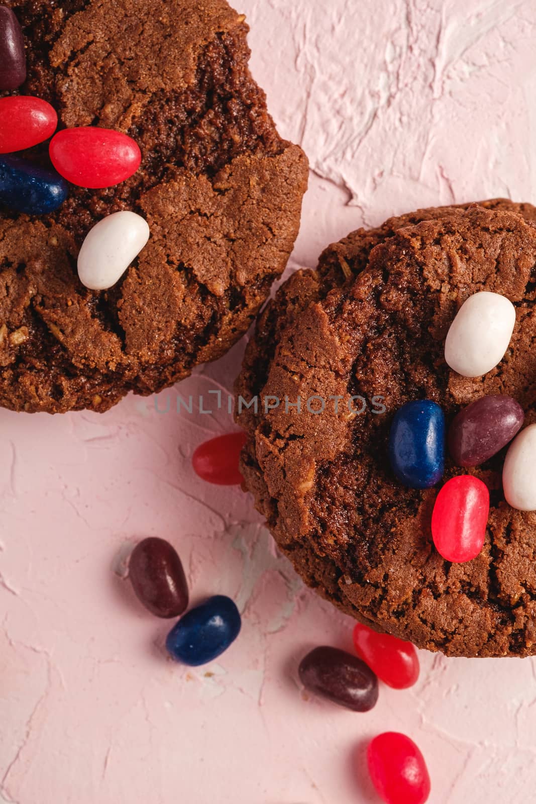 Homemade oat chocolate cookies with cereal with juicy jelly beans on textured pink background, top view macro