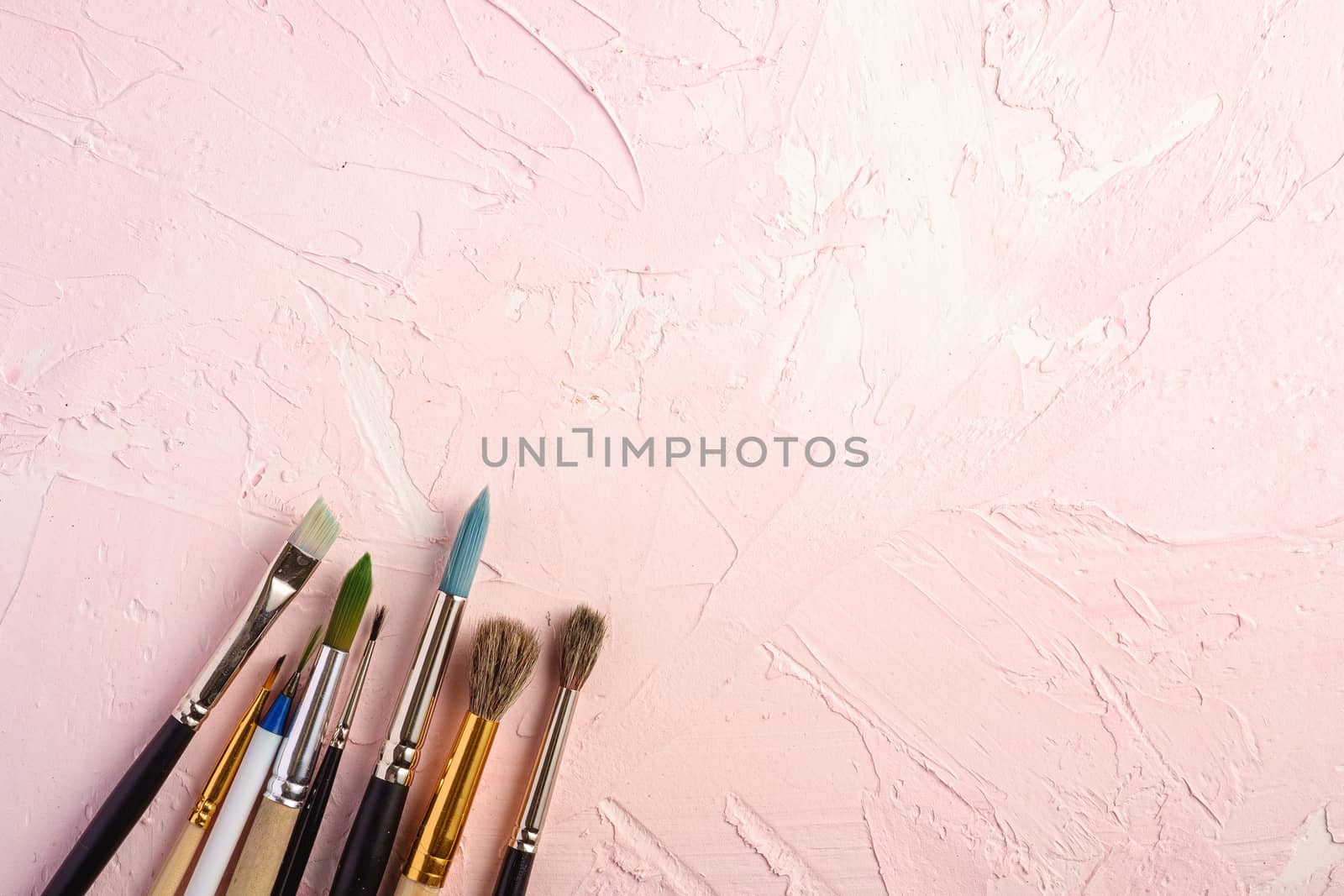 Paint brushes, artist tools for drawing on textured pink background, top view, copy space