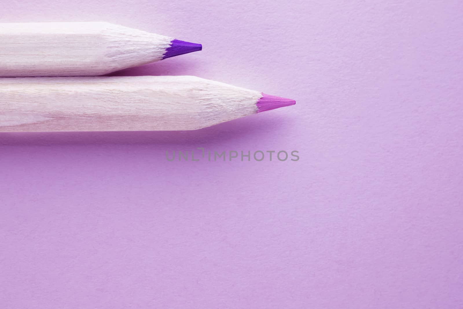 Two wooden  pencils on pink background ,pencils with pink and purple  points