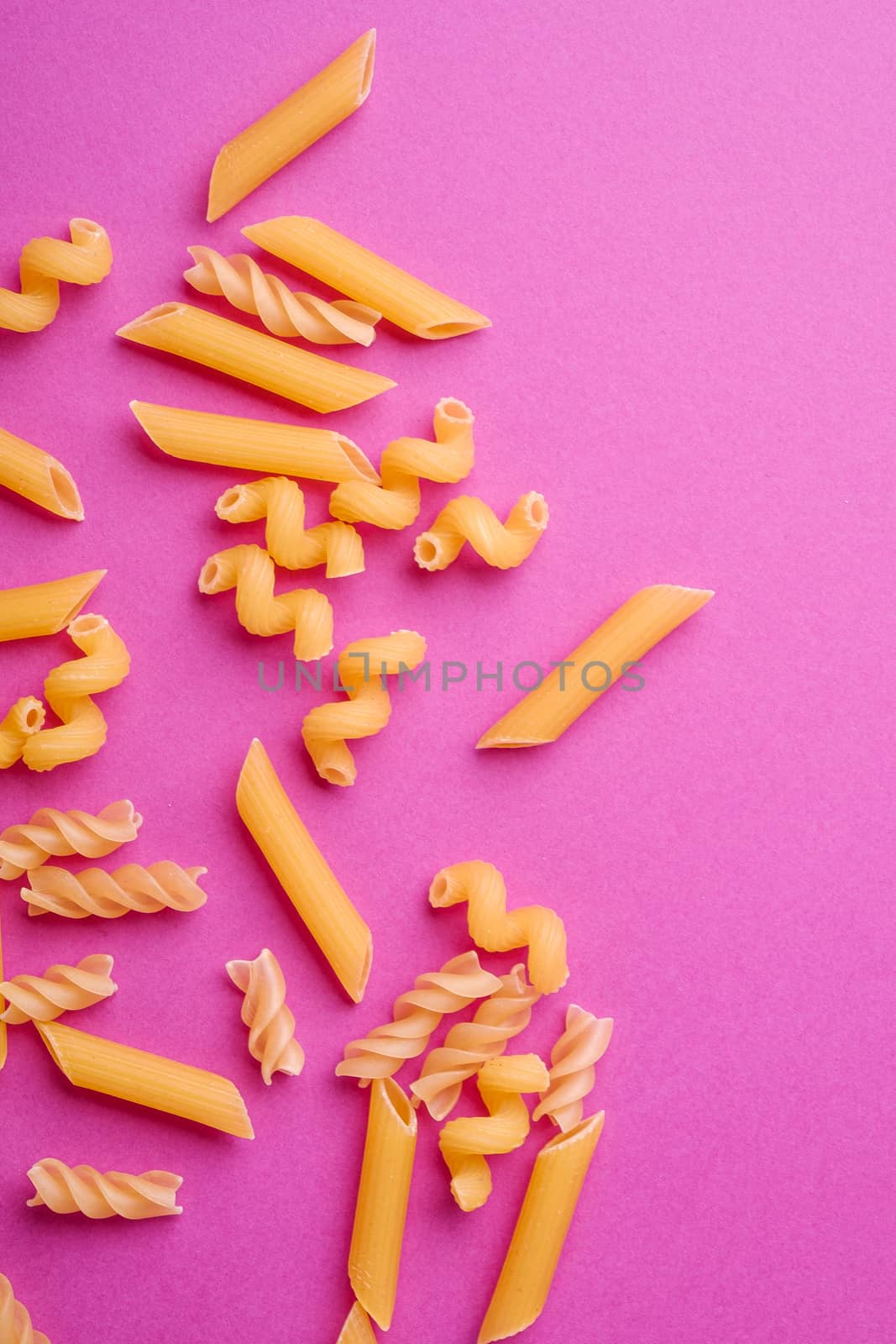Scattered variety of uncooked golden wheat pasta on minimal pink background, top view