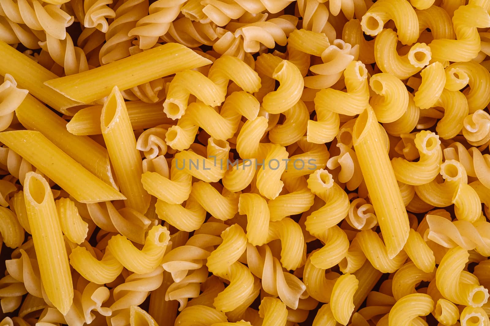 Texture of variety uncooked golden wheat pasta background, top view macro
