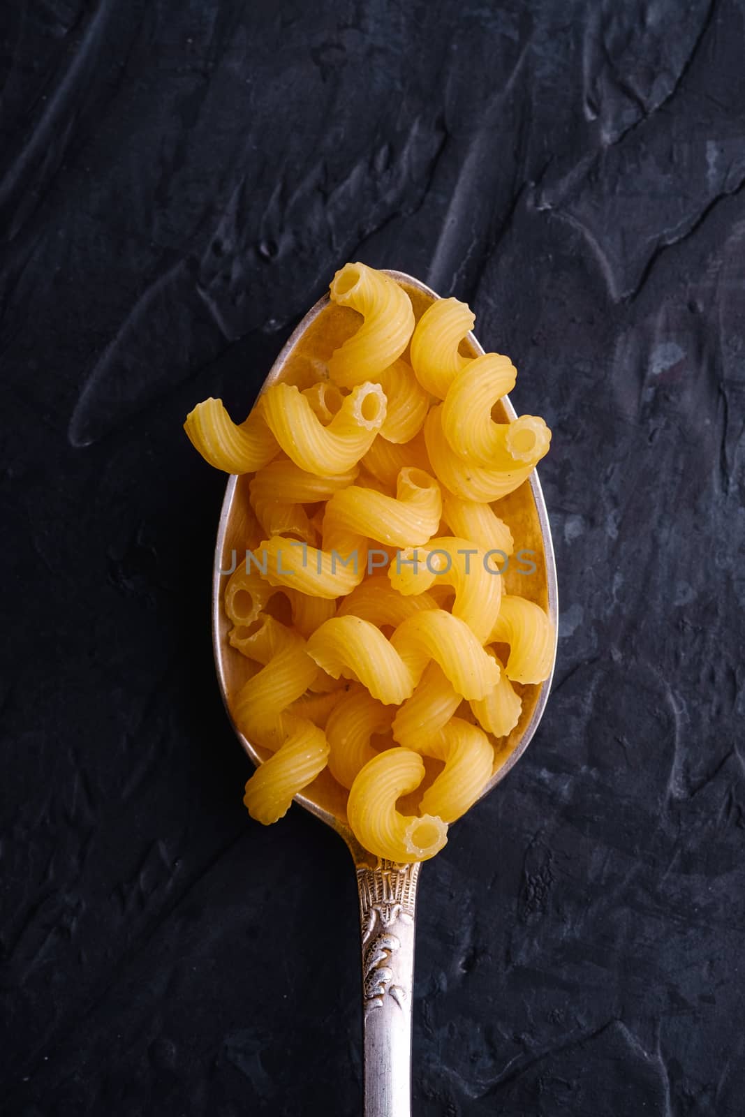 Cutlery spoon with cavatappi uncooked golden wheat curly pasta on dark textured background