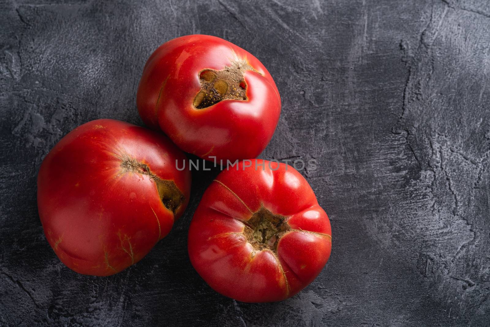 Three pink heirloom tomato vegetables, fresh red ripe tomatoes, vegan food, dark stone concrete background, top view