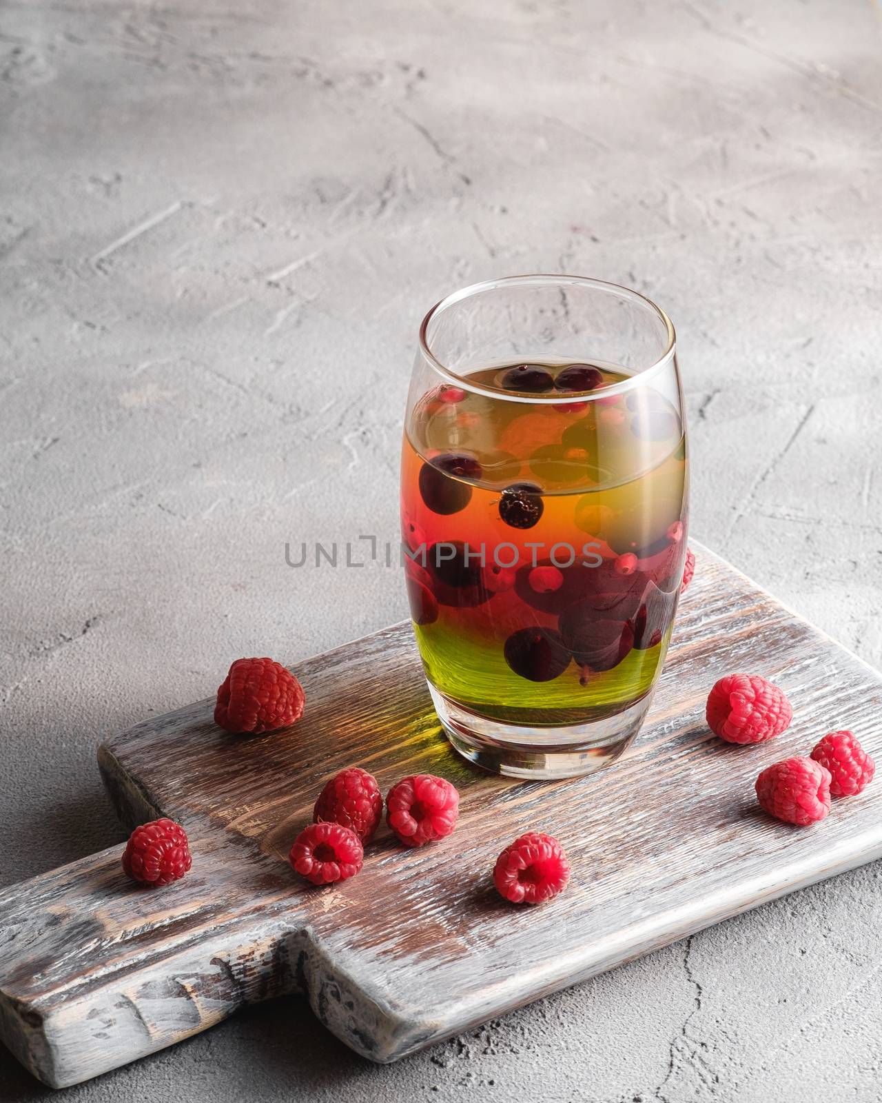 Jelly dessert with berries in glass on old wooden cutting board, sweet colorful layered pudding, stone concrete background, angle view