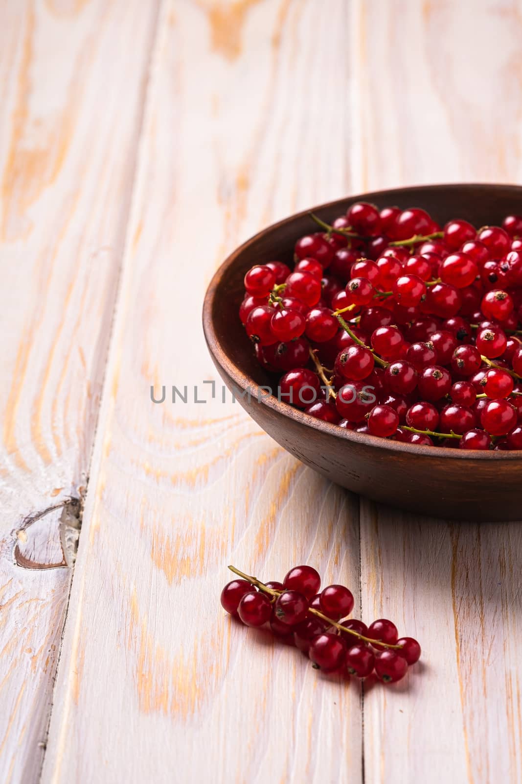 Fresh sweet red currant berries in wooden bowl, wood table background, angle view