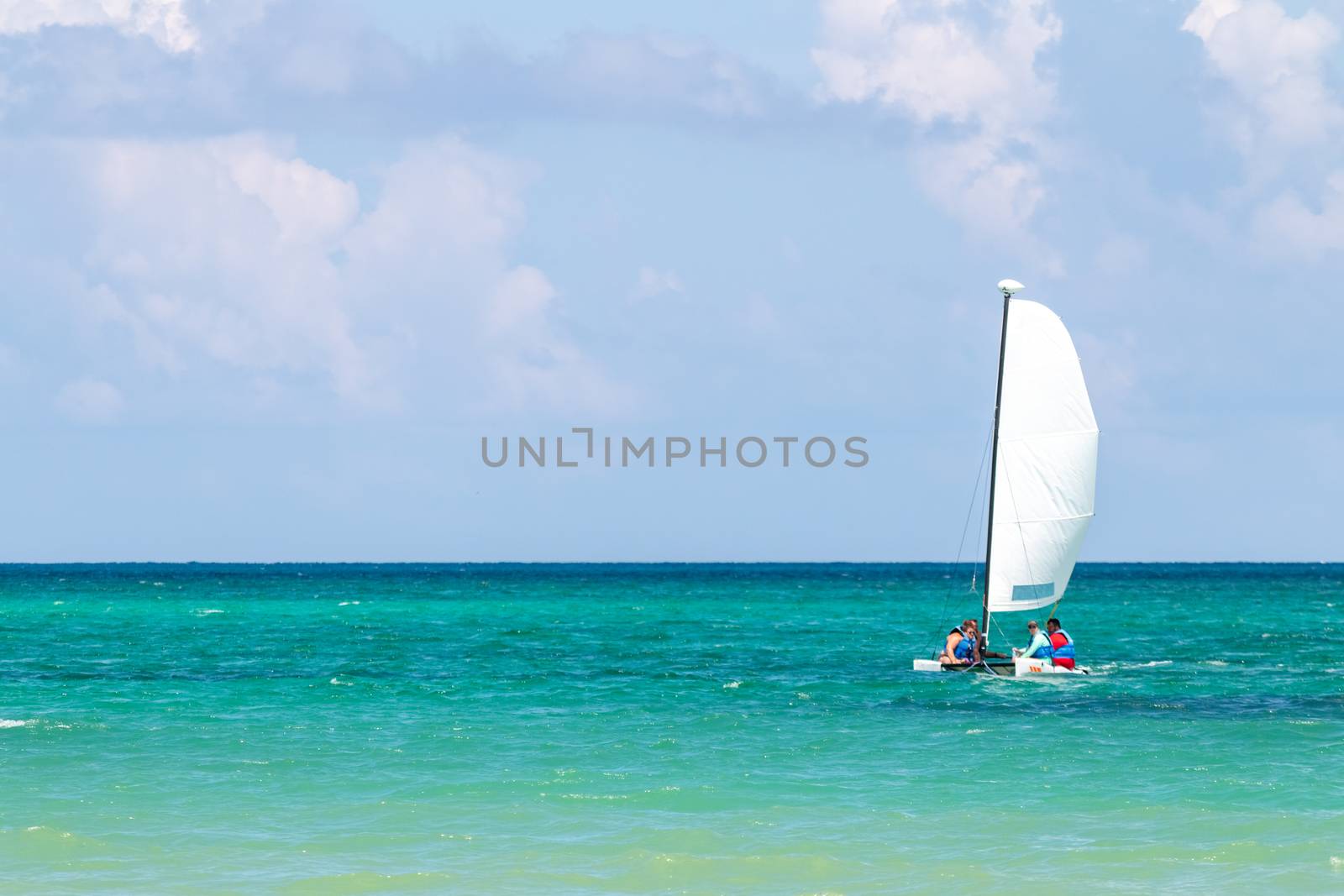 Nautical background of a white sailboat in bright sunlight, on blue ocean water, with space for text on left