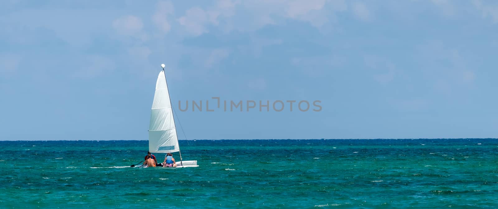 Nautical background of a white sailboat in bright sunlight, on blue ocean water, with space for text by leo_de_la_garza