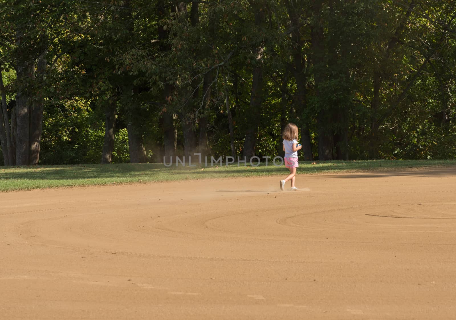 Small toddler girl playing in the sand and dirt of an empty baseball field in the infield area
