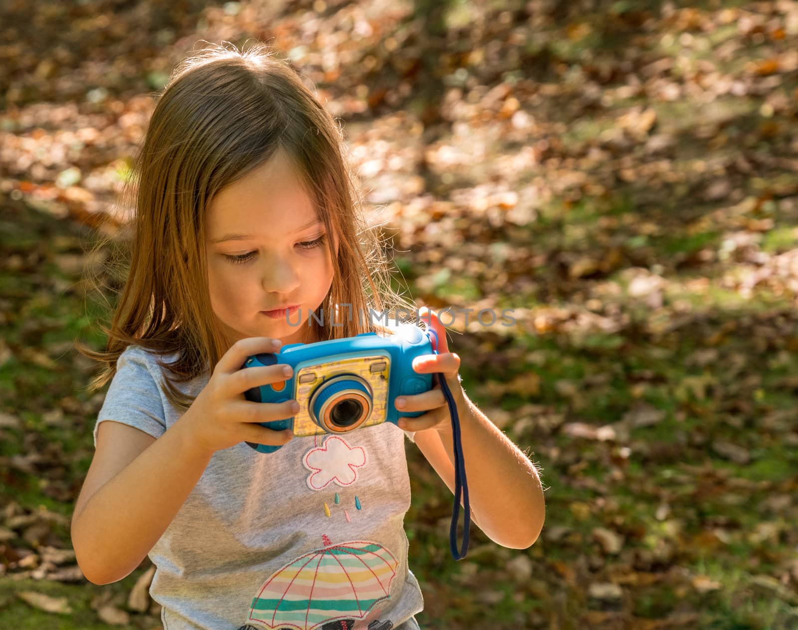 Small caucasian girl in a forest checking her photo on the back of a toy digital camera in concentration