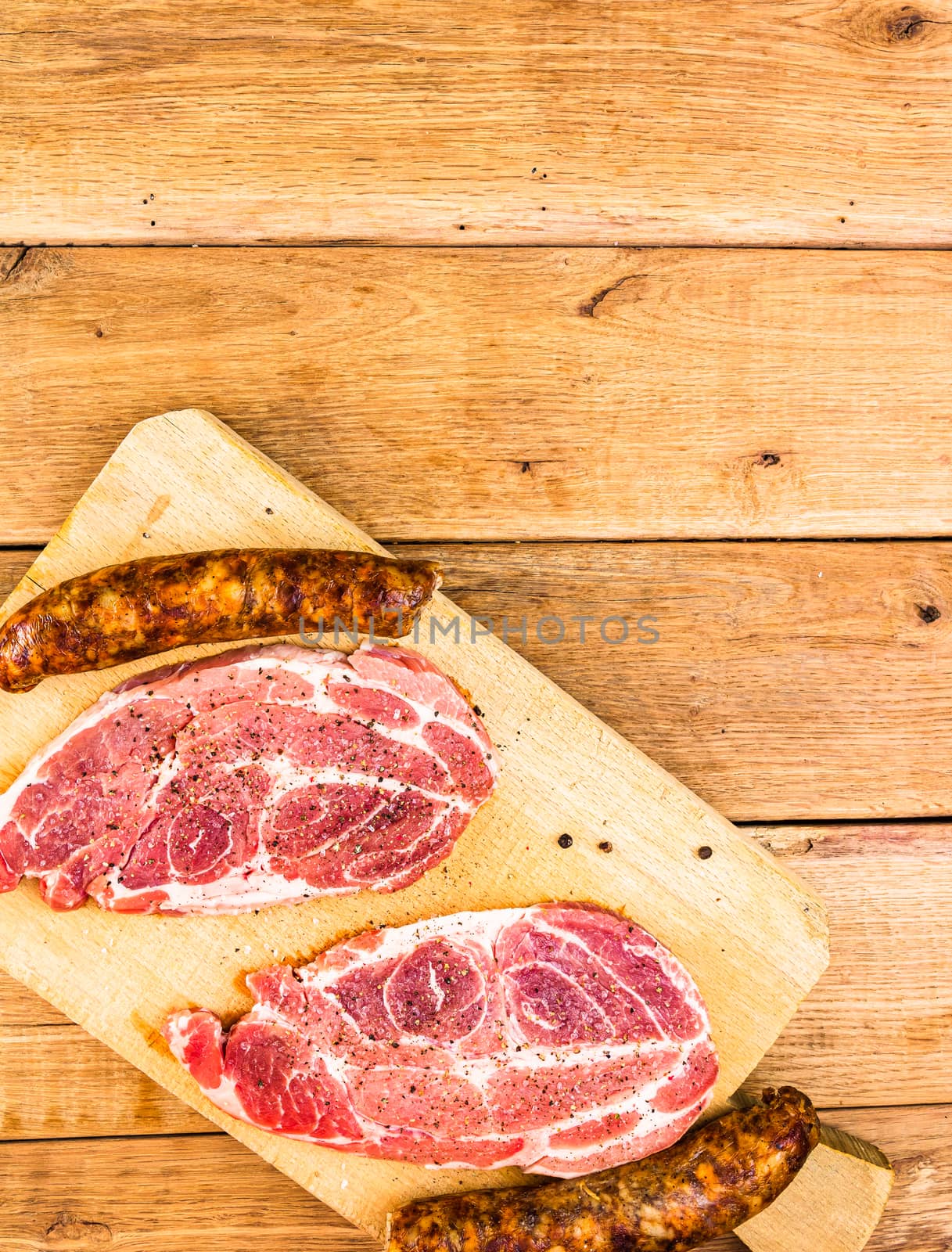 Pork chops with condiments and smoked sausage on a wooden cutting board over wooden table, meat for bbq, top view, copy space, barbeque concept