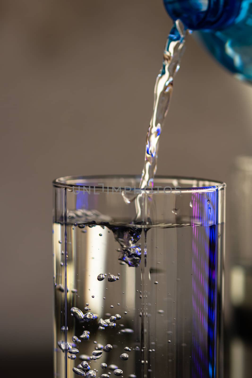 Pouring water from blue plastic bottle into a glass on blurred background. Selective focus, shallow DOF and copy space