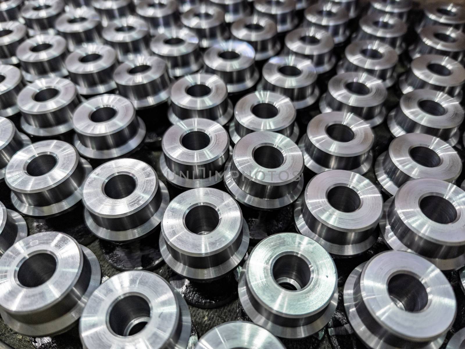 batch of shiny round steel parts background, close-up with selective focus and blur.