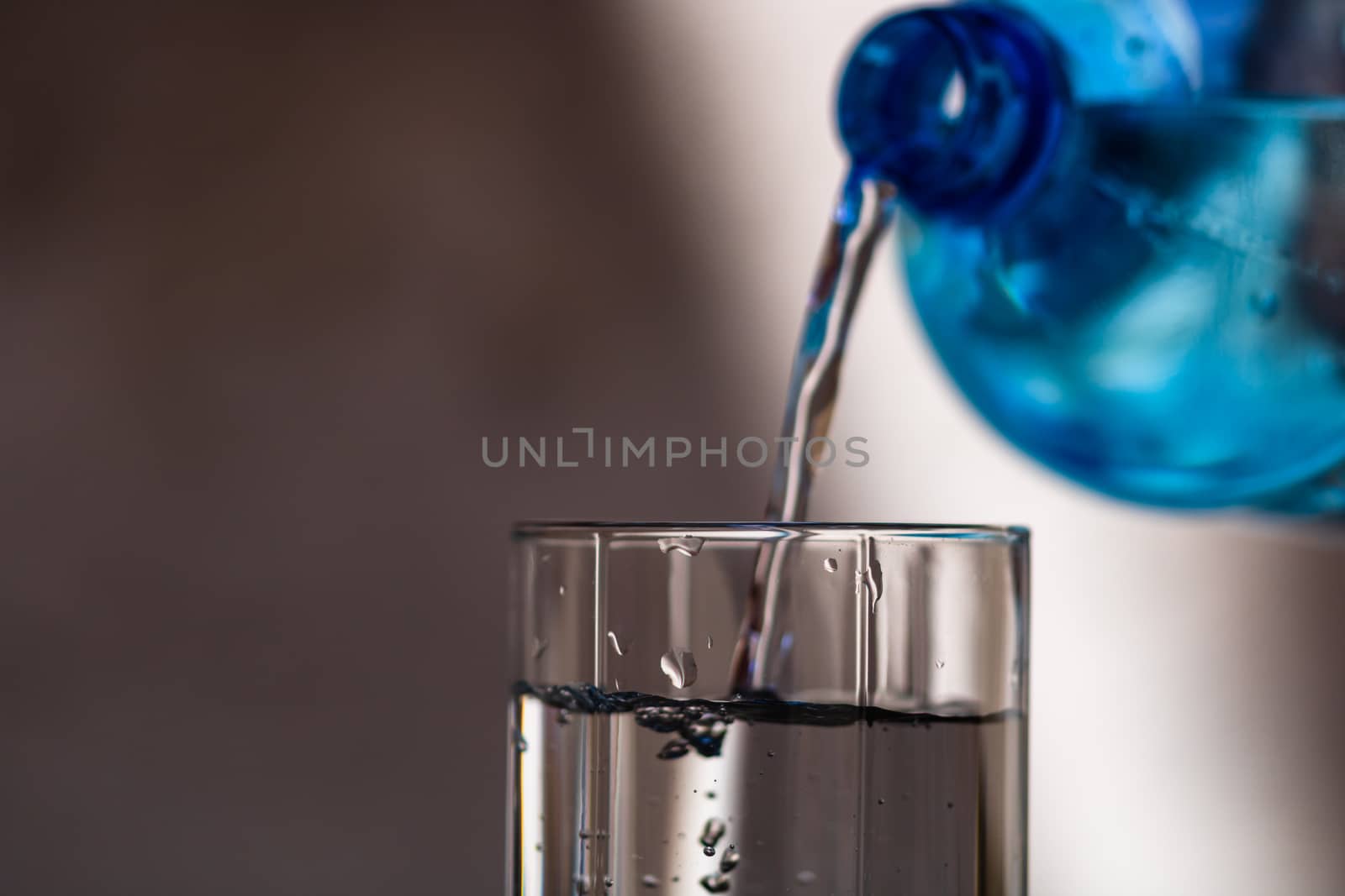 Pouring water from blue plastic bottle into a glass on blurred background. Selective focus, shallow DOF and copy space