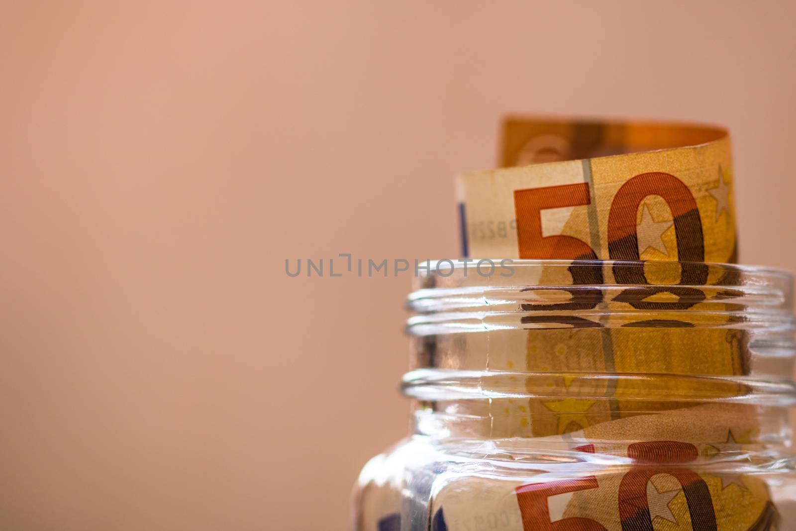 Composition with saving money banknotes (50 EURO) in a glass jar. Concept of investing and keeping money, close up isolated.