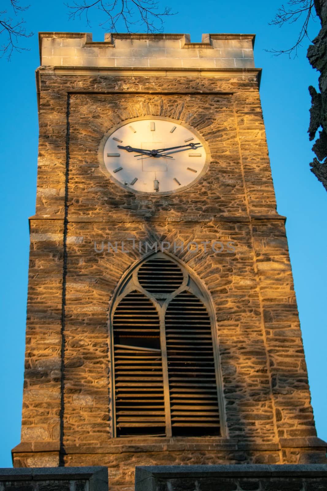 A Clocktower bathed in glowing orange sunlight with shadows from a tree