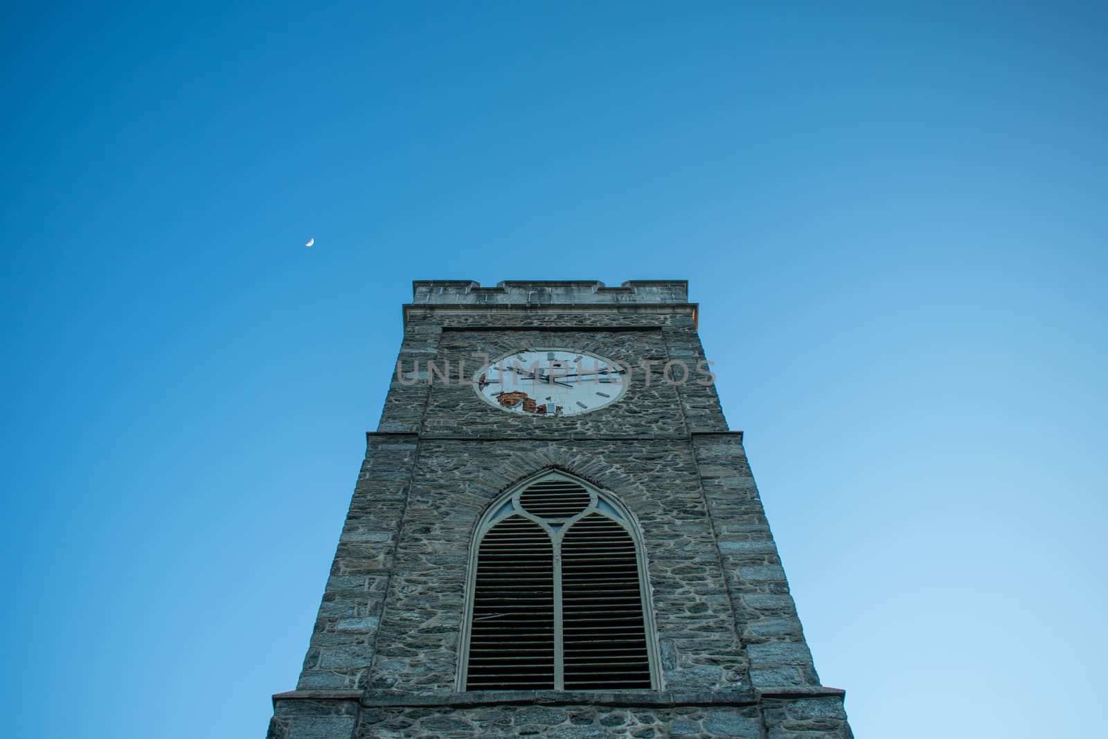 A Church's Cobblestone Clock Tower on a Clear Blue Sky