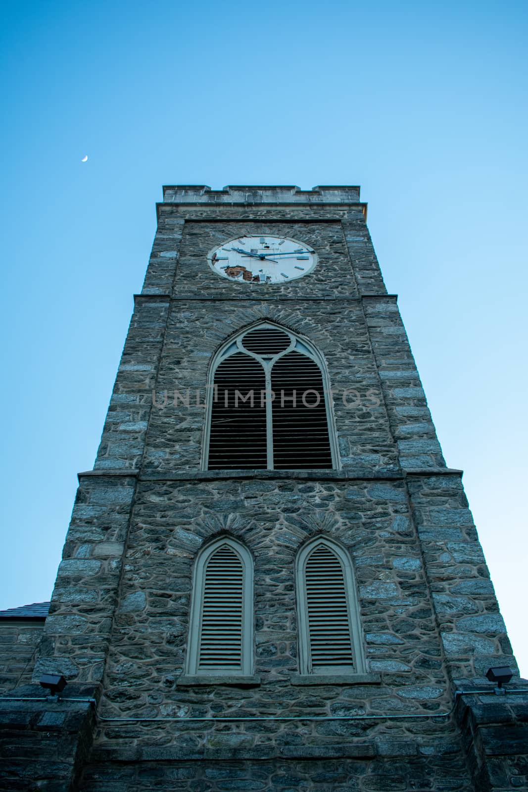 A Church's Cobblestone Clock Tower on a Clear Blue Sky