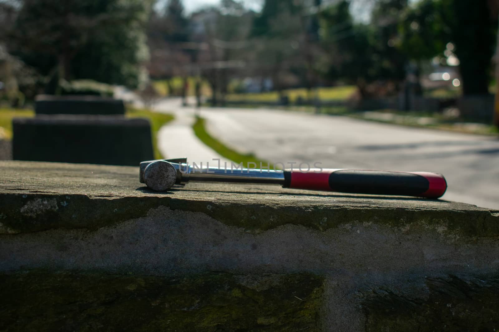 A Hammer With a Red and Black Handle on a Cobblestone Pillar on a Suburban Street