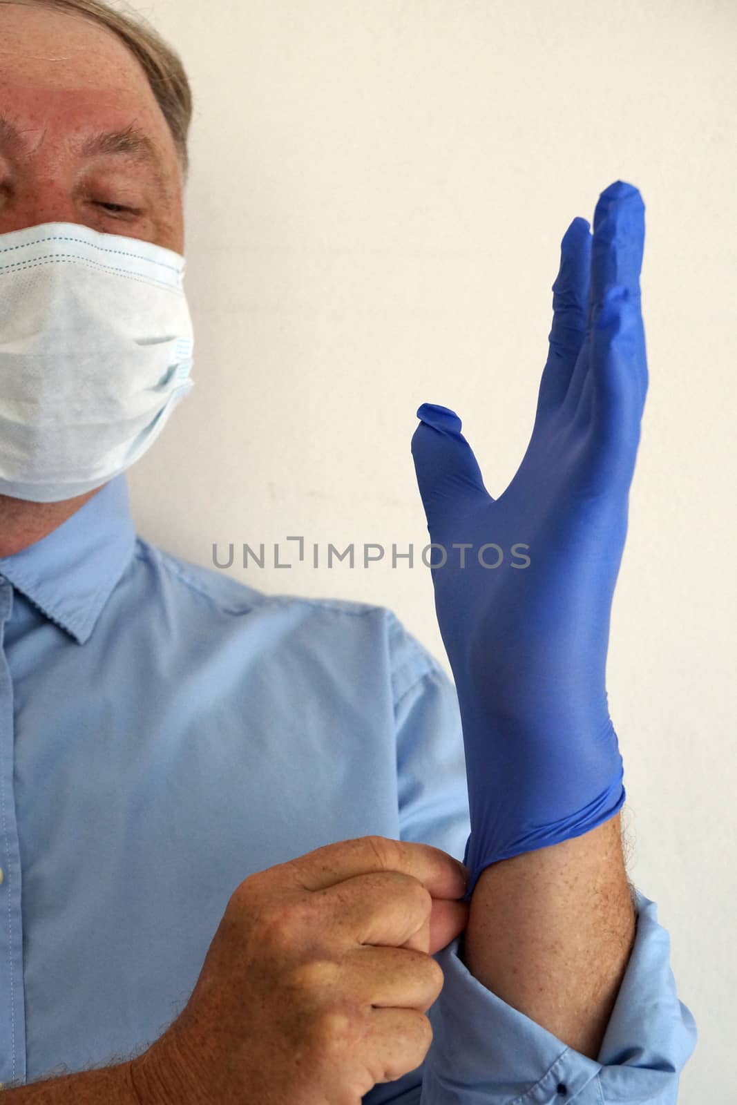 masked doctor puts on medical gloves close up by Annado