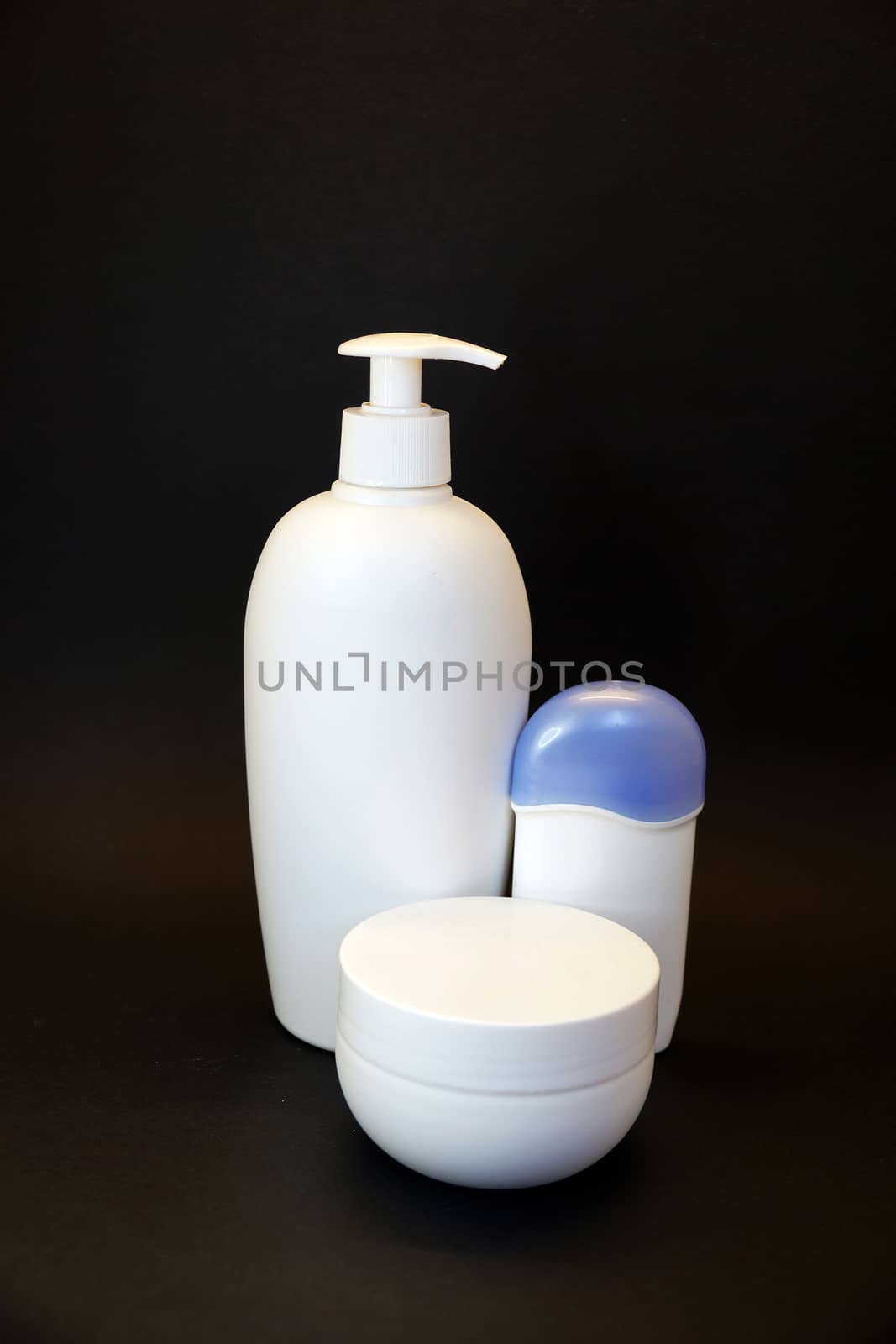 cosmetic white bottle with spray bottle, cream jar and deodorant on black background. by Annado