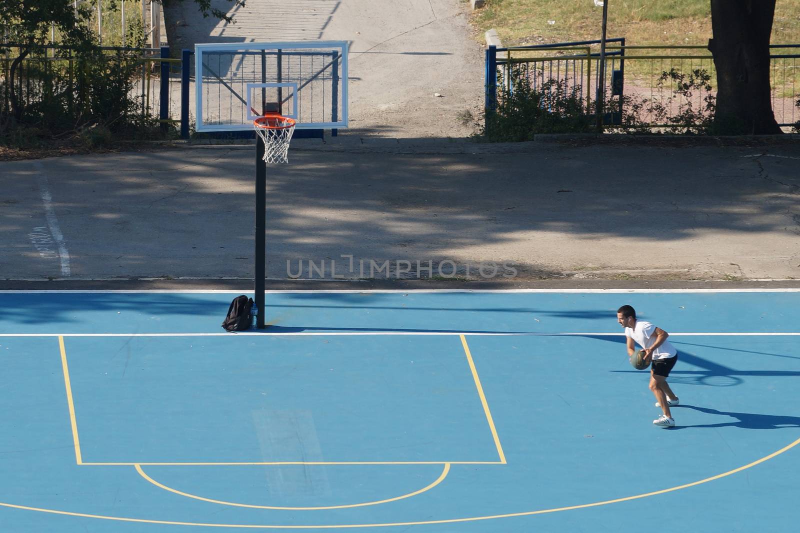 Varna, Bulgaria - August, 22, 2020: young man training with a ball on an outdoor basketball court