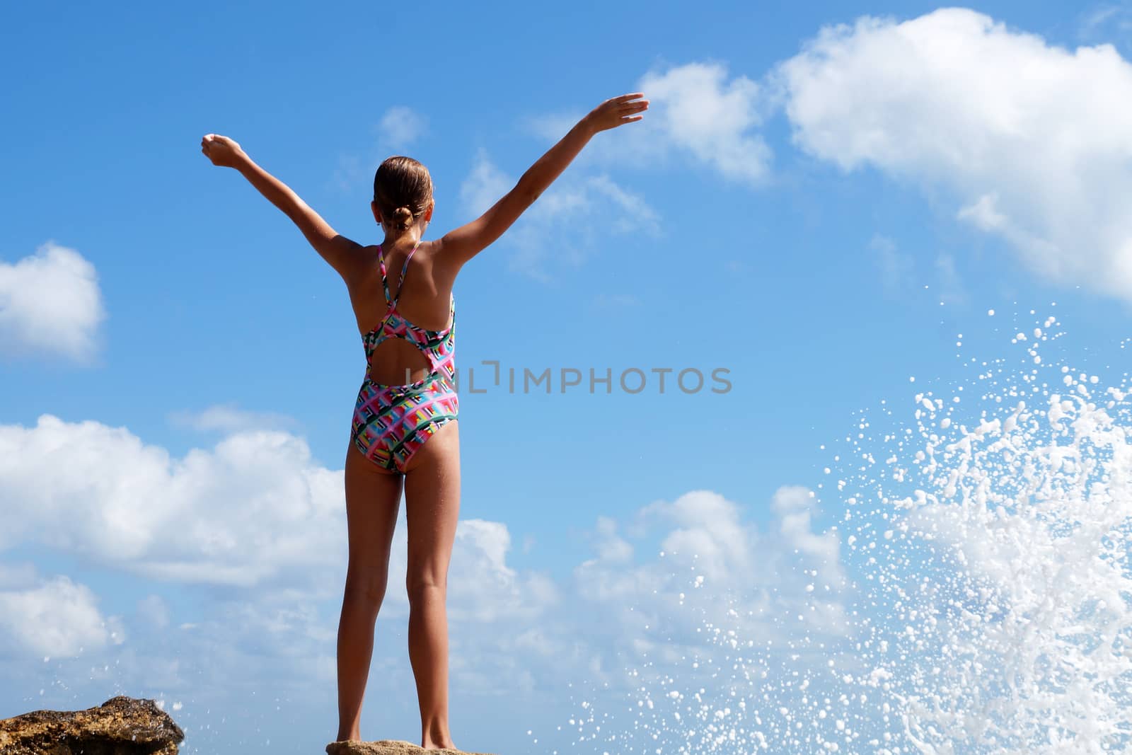 teenage girl stands in raised hands on a stone by the sea, copy space