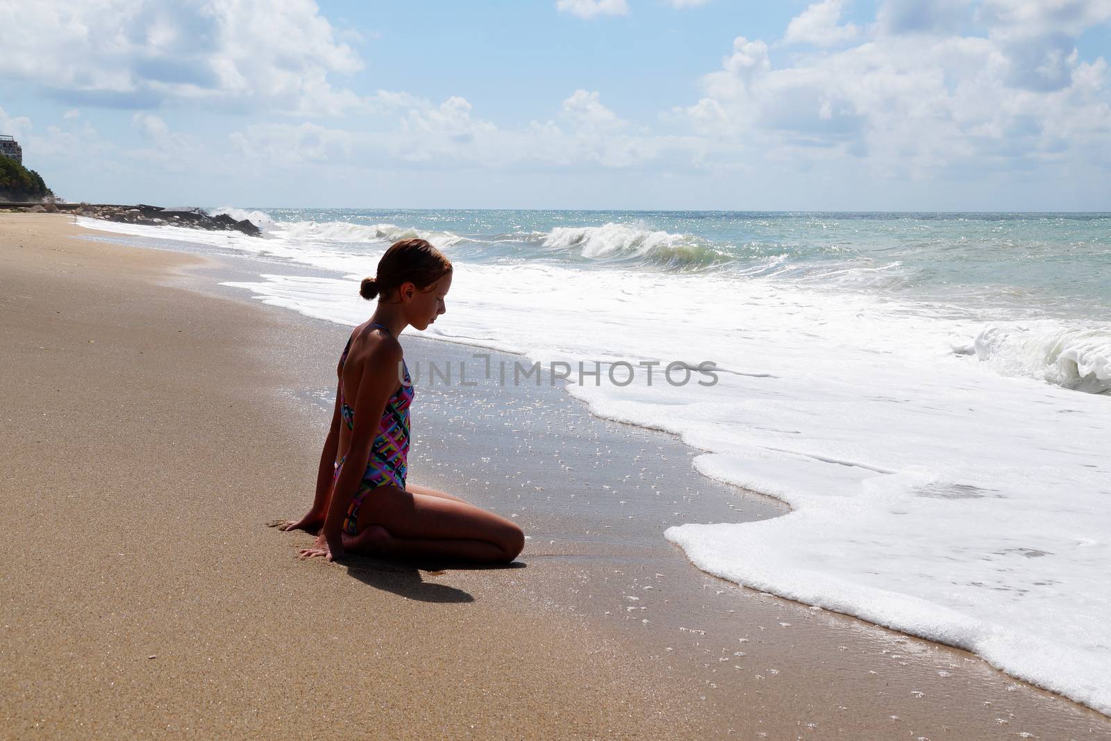 teenage girl sitting on the sand by the sea by Annado