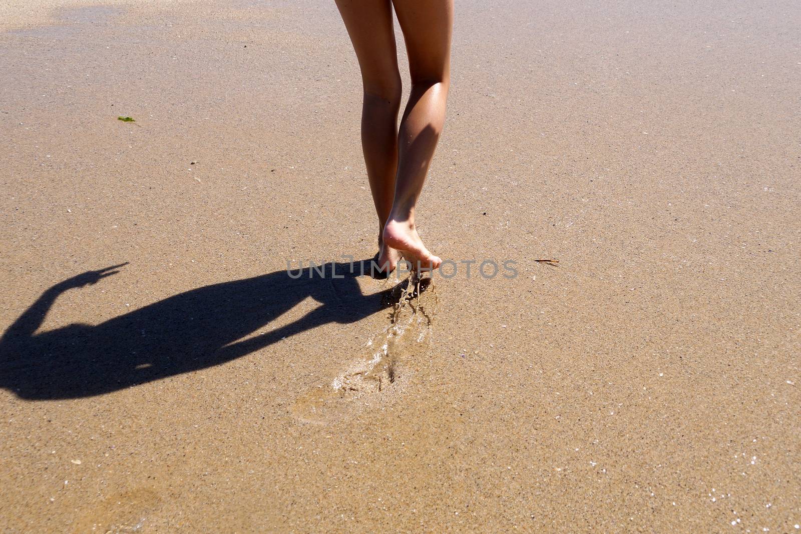 child feet walk on wet sea sand, back view.