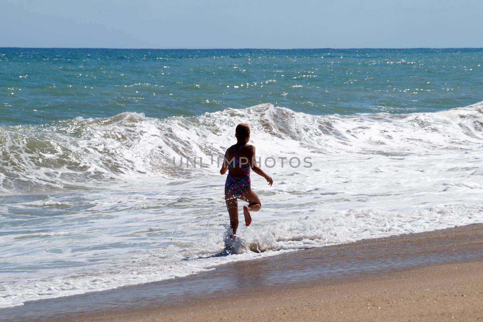 teenage girl happily runs along the sandy seashore next to the big waves.