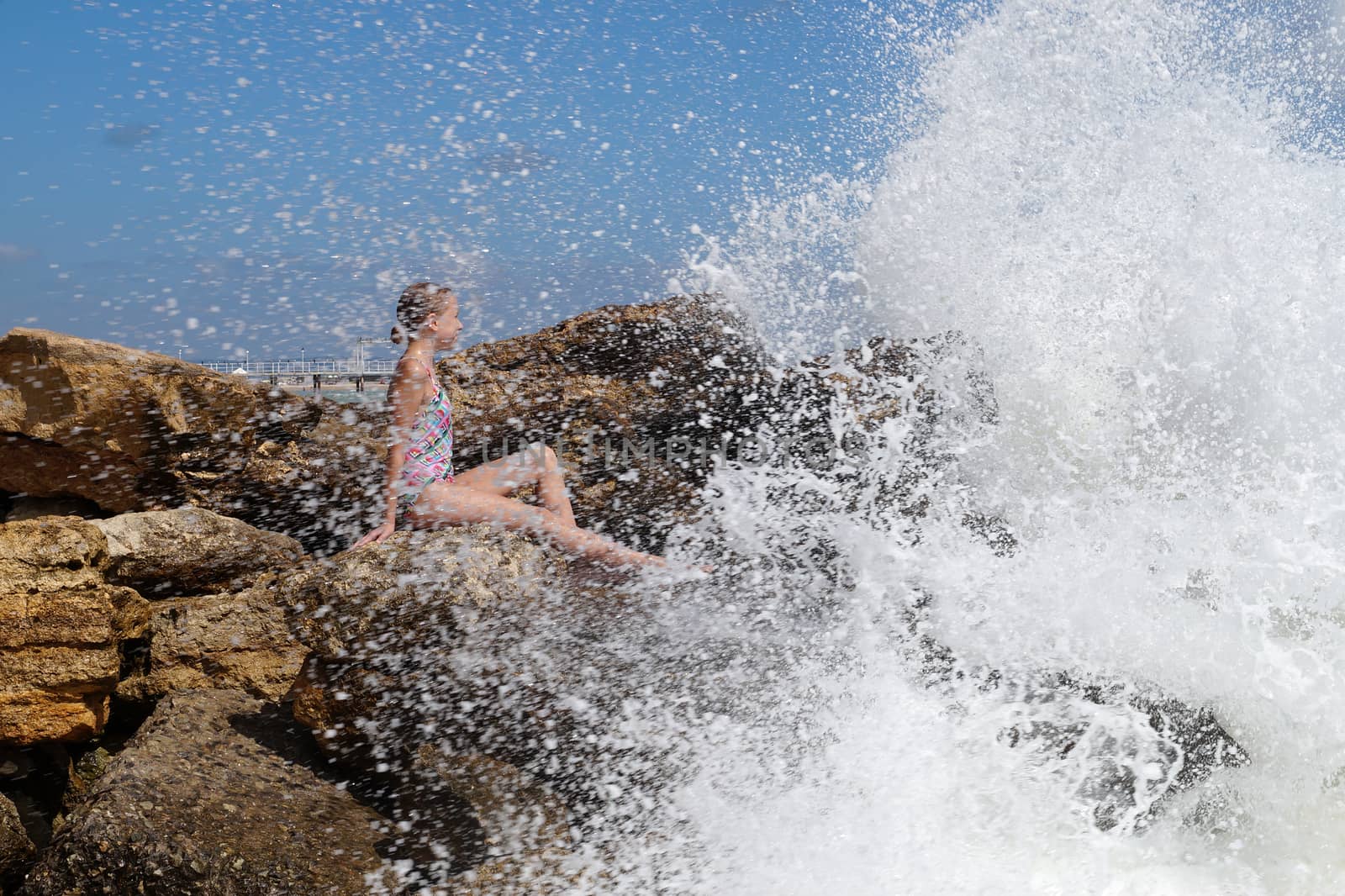 teenage girl sitting on a stone on the seashore under the splashing waves.