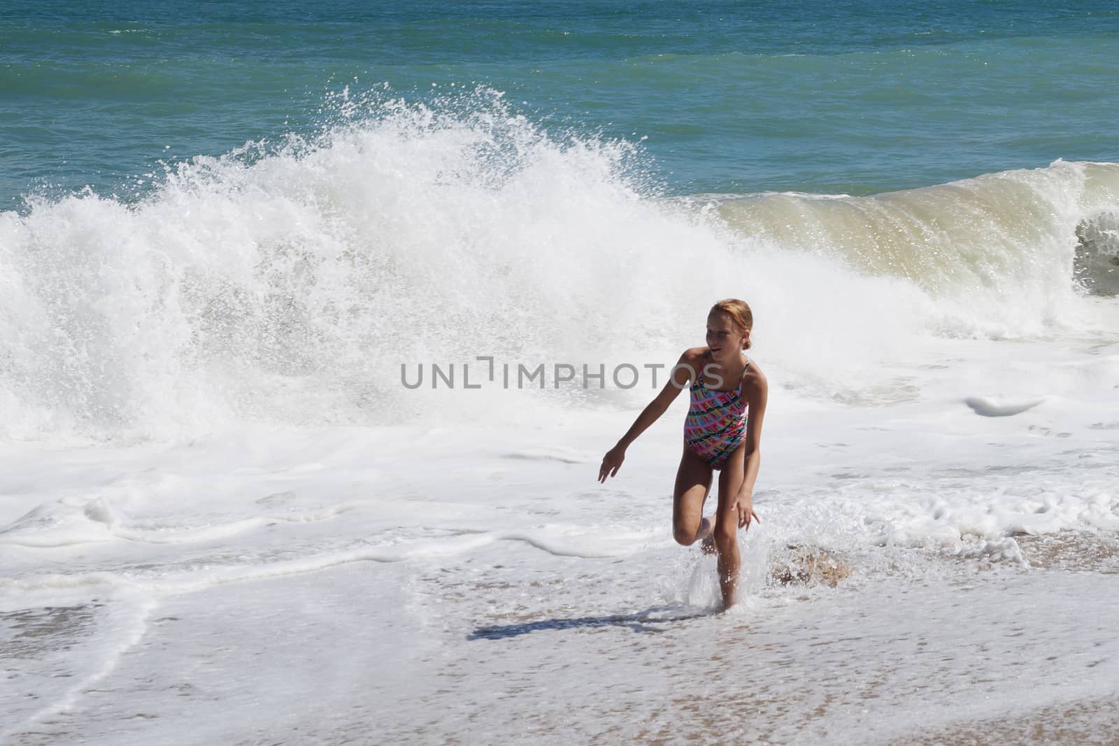 teenage girl happily runs along the sandy seashore next to the big waves by Annado