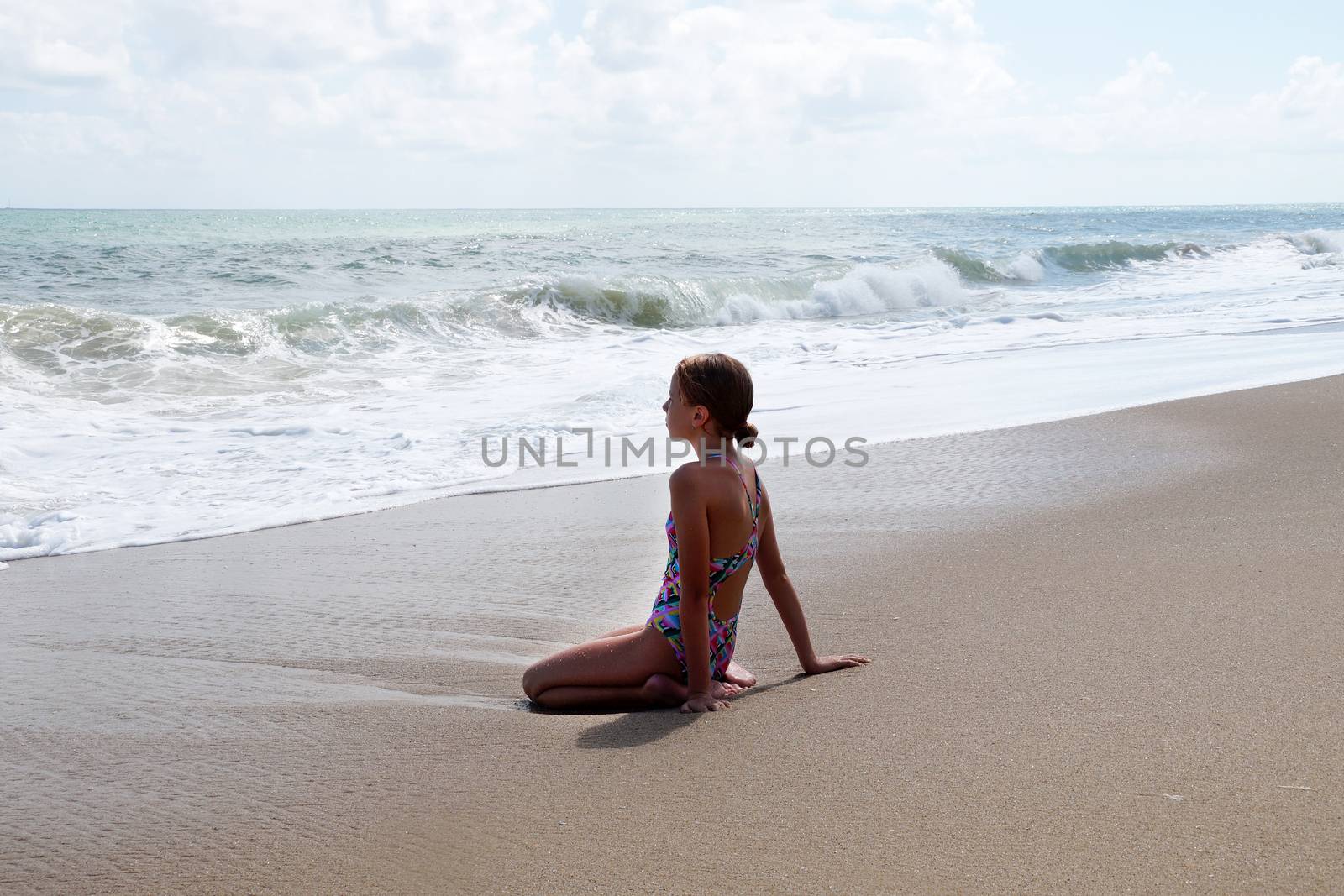 teenage girl sitting on the sand by the sea.