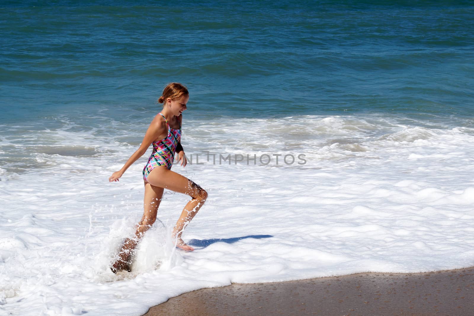 teenage girl happily runs along the sandy seashore next to the big waves by Annado