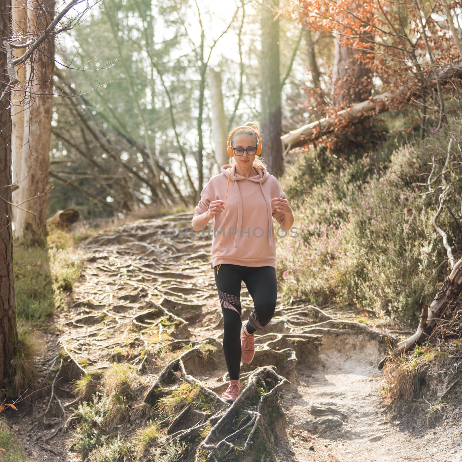 Active sporty woman listening to the music while running in autumn fall forest. Female runner training outdoor. Healthy lifestyle image of young caucasian woman jogging outside.