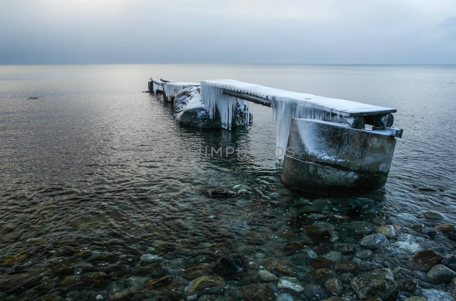 Wooden pier in sea covered with ice and snow with icicles.