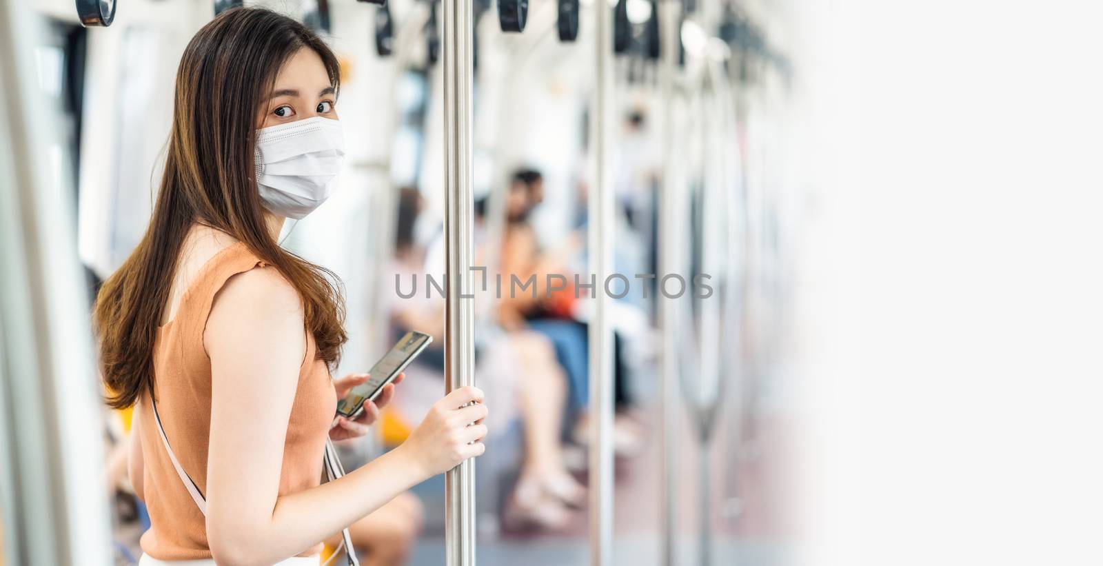 Young Asian woman passenger wearing surgical mask and looking at camera in subway train when traveling in big city at Covid19 outbreak, Infection and Pandemic, social distancing and new normal concept