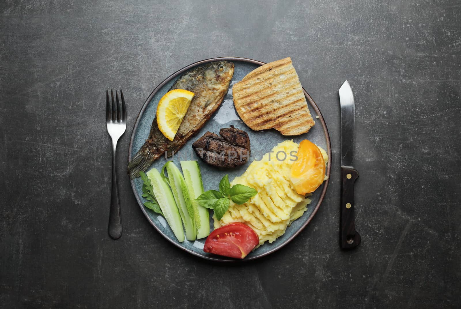 Fried fish, meat steak and vegetables on a plate. Concrete gray countertop. High quality photo