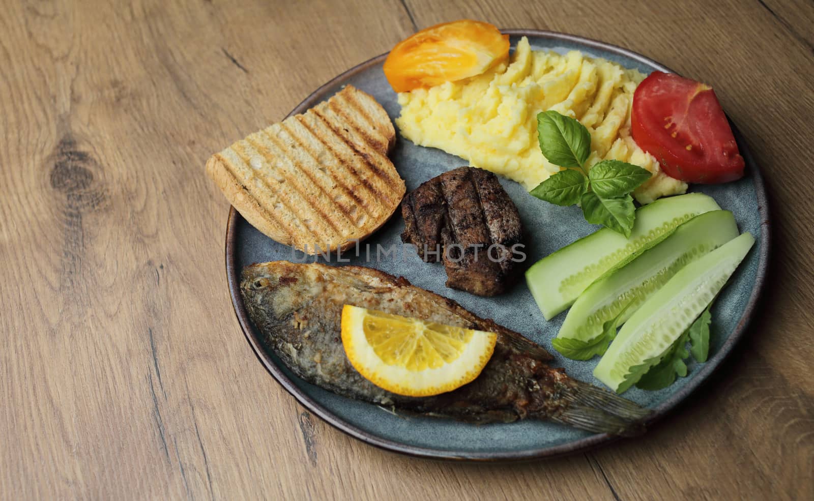 Fried fish, meat steak and vegetables on a plate. On a wooden table by selinsmo