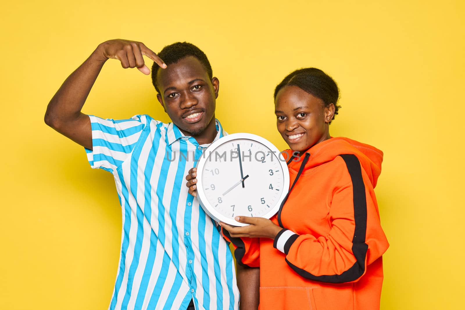 Young couple of african appearance holding a watch in yellow hands isolated background dating family