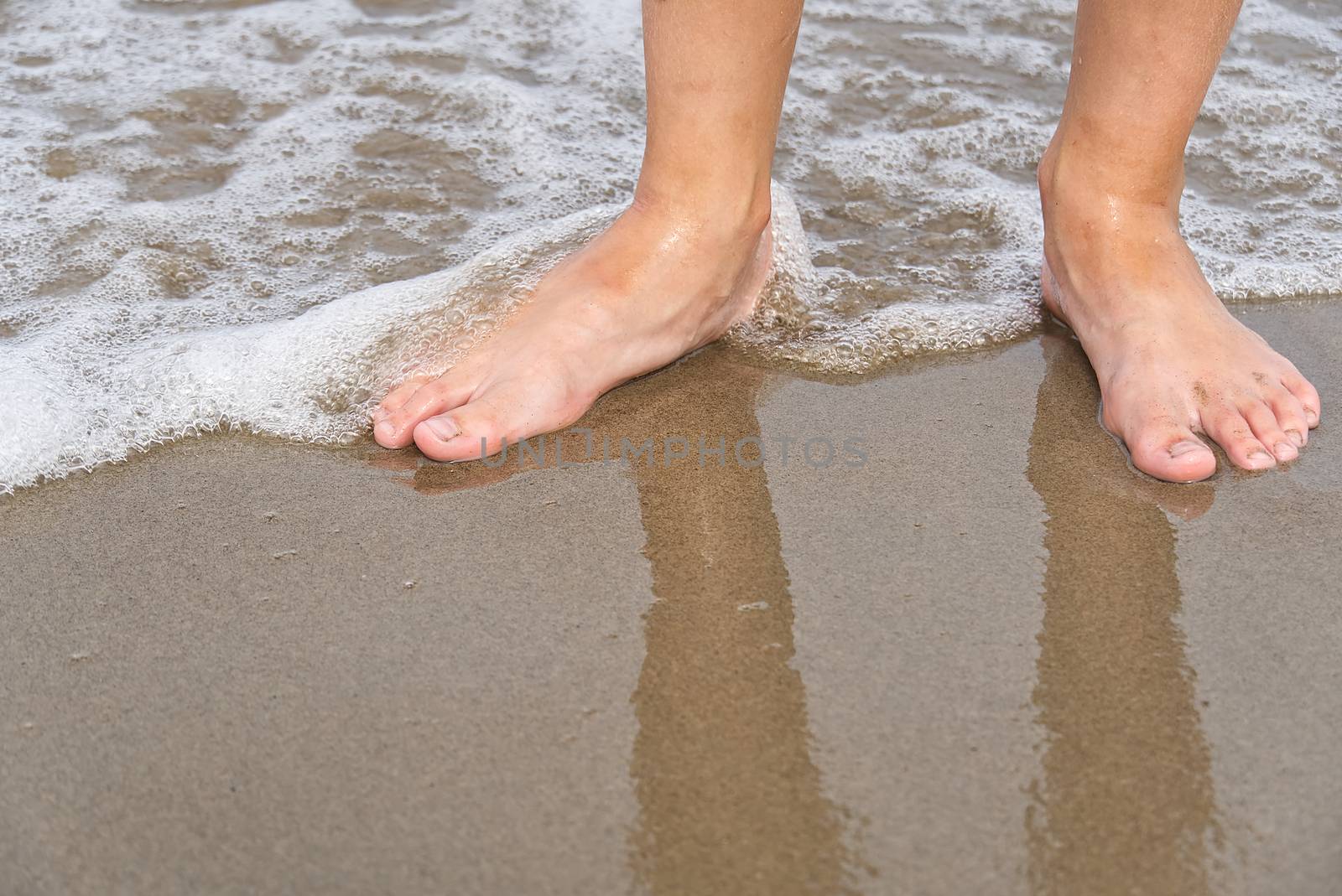 Close-up of child's legs walking on sand coast and sea water. Young girl legs on baltic sea beach. Teenager legs near sea line. by PhotoTime