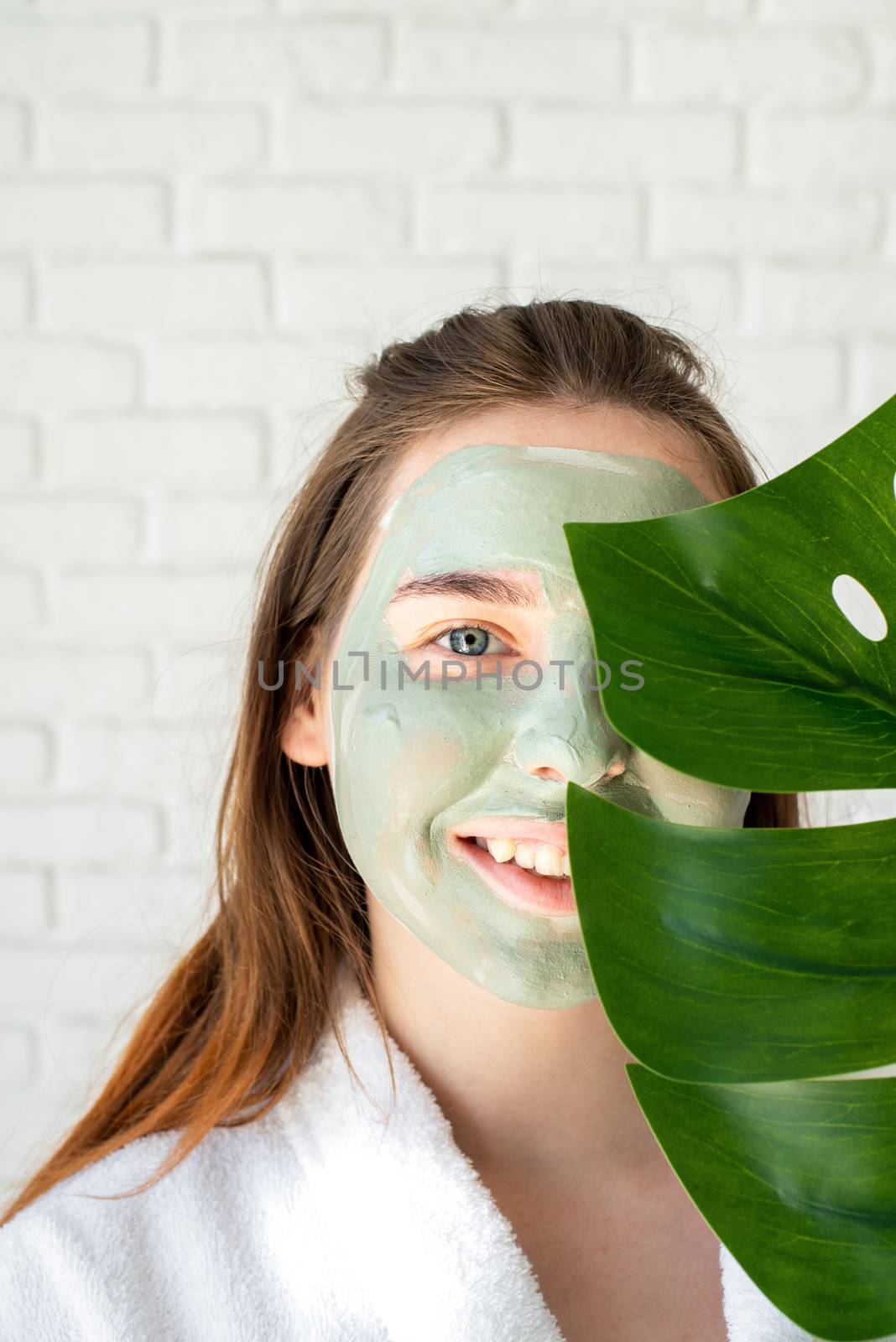 Portrait of a happy young woman with a facial mask holding a monstera leaf by Desperada