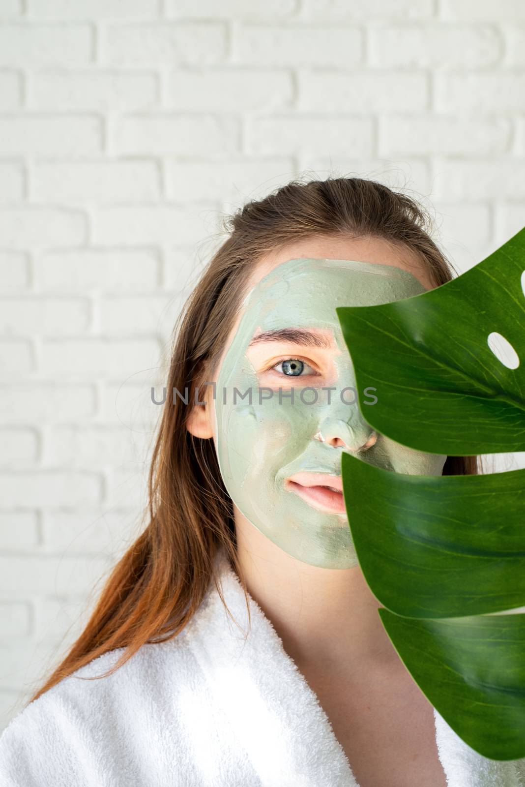 Portrait of a happy young woman with a facial mask holding a monstera leaf by Desperada