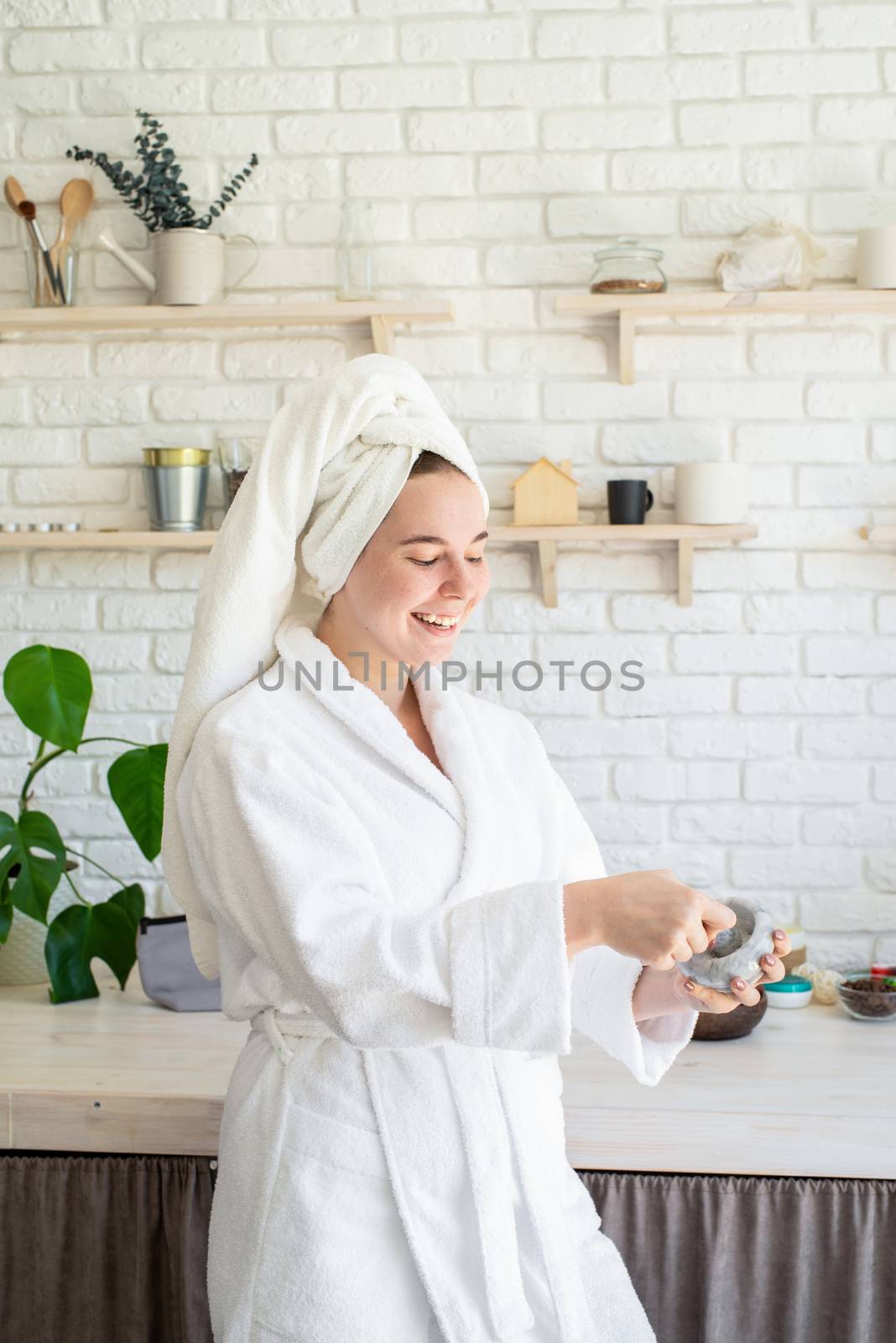 Happy young woman applying face scrub on her face in her home kitchen by Desperada