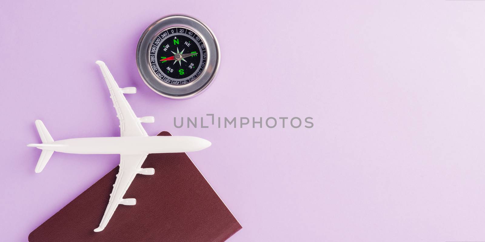 World Tourism Day, minimal toy model plane, passport and compass, studio shot isolated on a purple background with copy space for text, holiday travel concept
