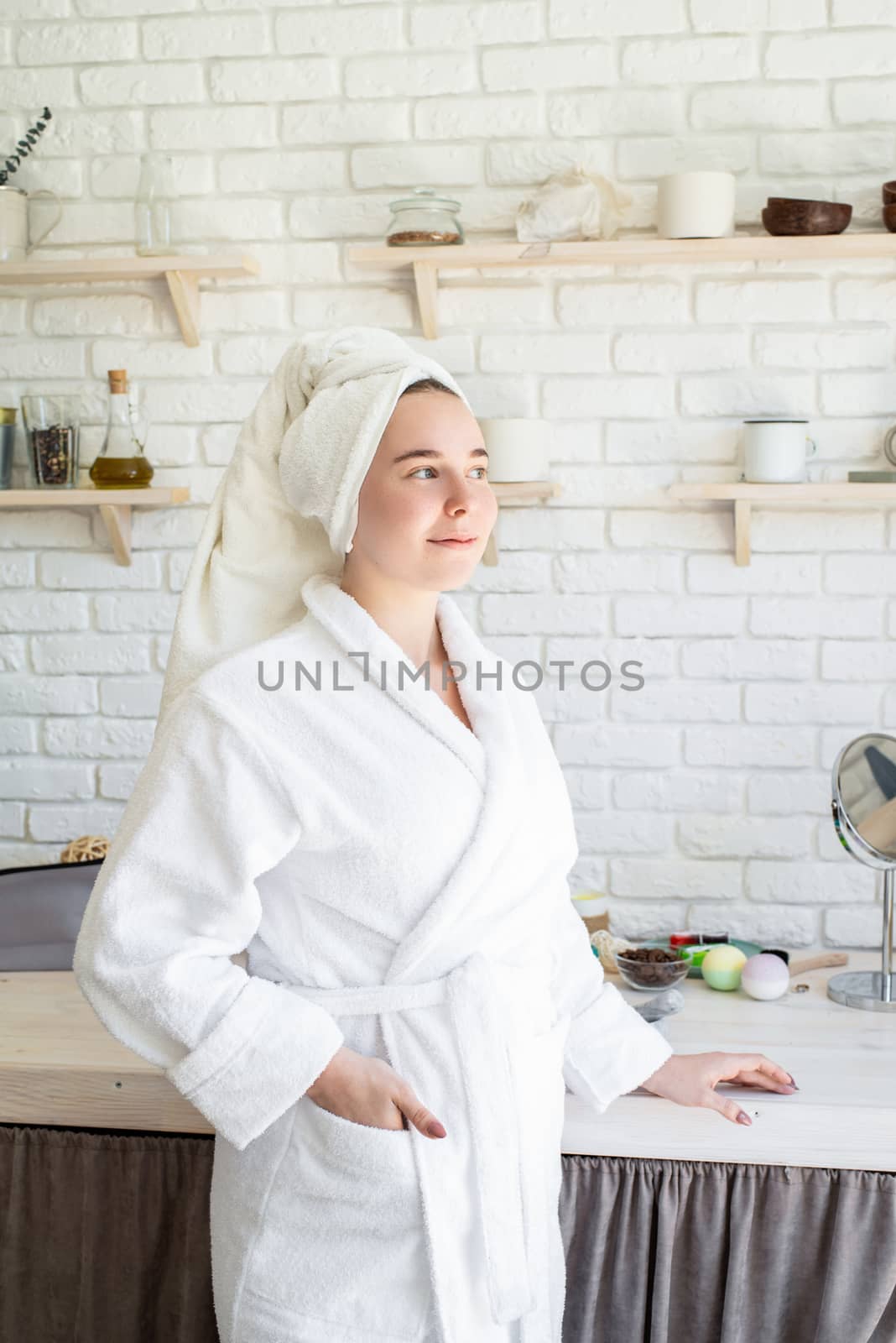 Happy young woman applying face scrub on her face in her home kitchen by Desperada