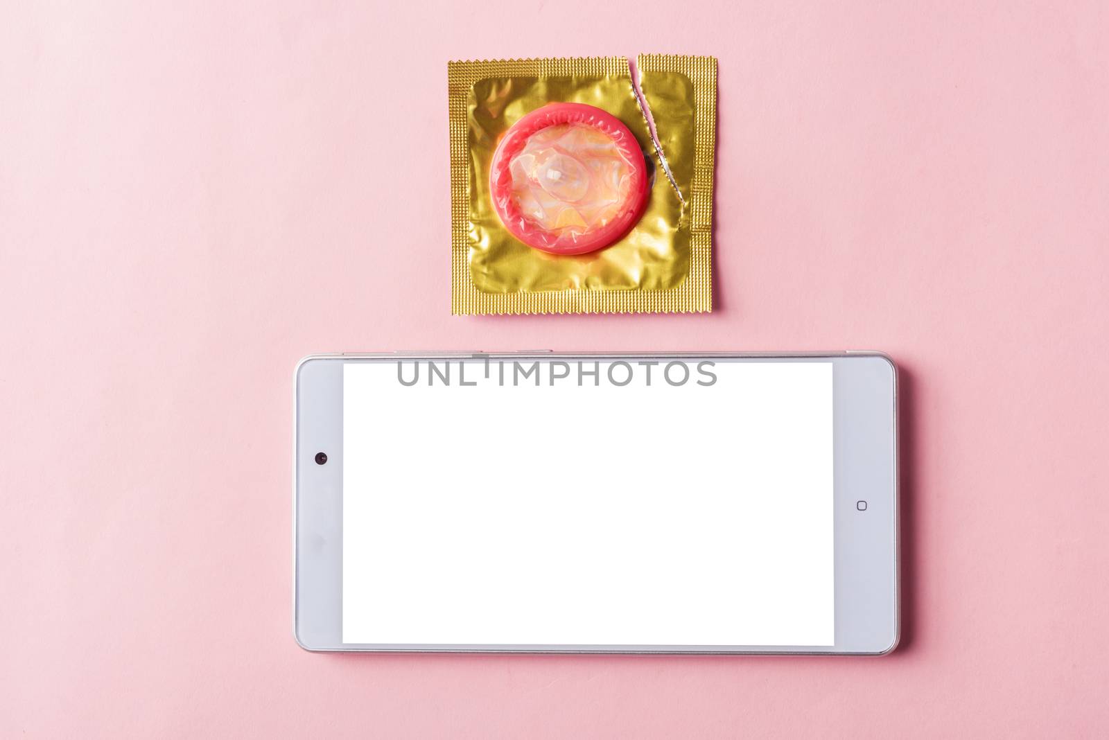 World sexual health or Aids day, Top view flat lay condom in wrapper pack and smart mobile phone blank screen, studio shot isolated on a pink background, watching porn content on mobile phone concept