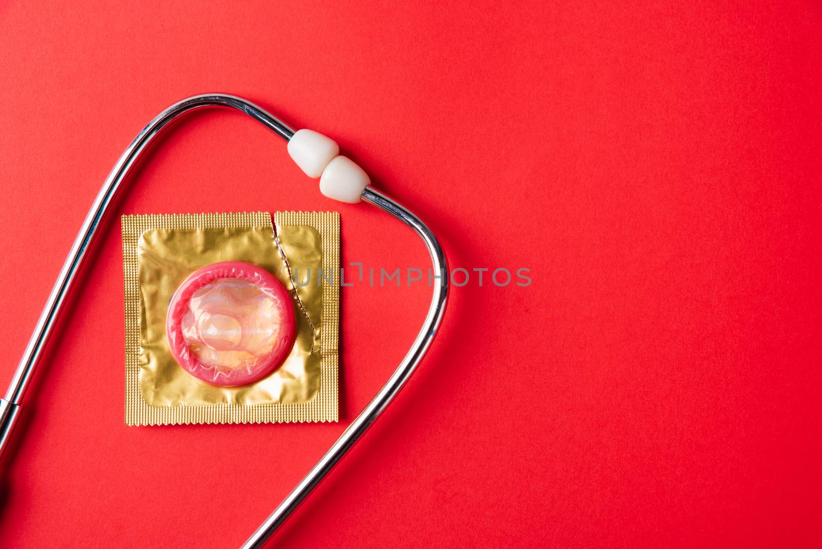 World sexual health or Aids day, Top view flat lay medical equipment, condom in pack and stethoscope, studio shot isolated on a red  background, Safe sex and reproductive health concept